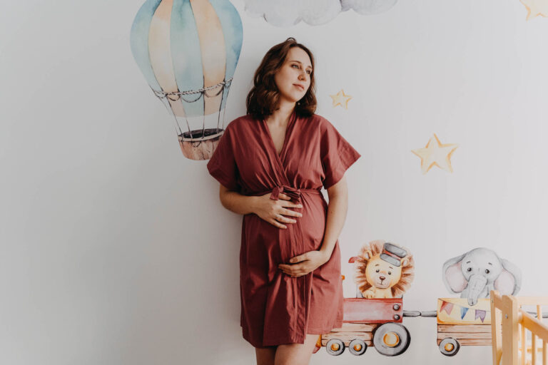 Jak się ubrać na sesje ciążową, kobieta w ciąży na tle ściany z tapetą w pokoju dziecka
